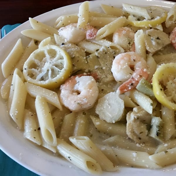 Penne pasta with shrimp, scallops, lemon slices, and herbs in a creamy white sauce.