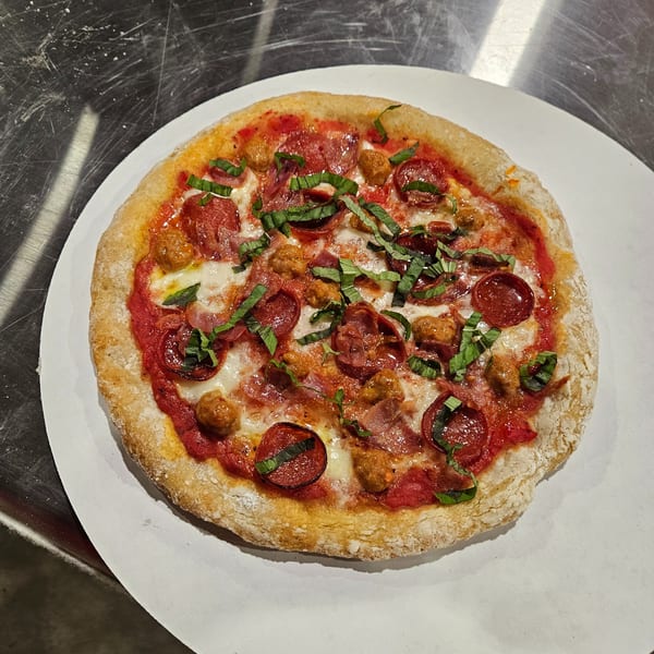 A Little Pizza Heaven's Italian pizza with pepperoni, sausage, and basil on a white plate.