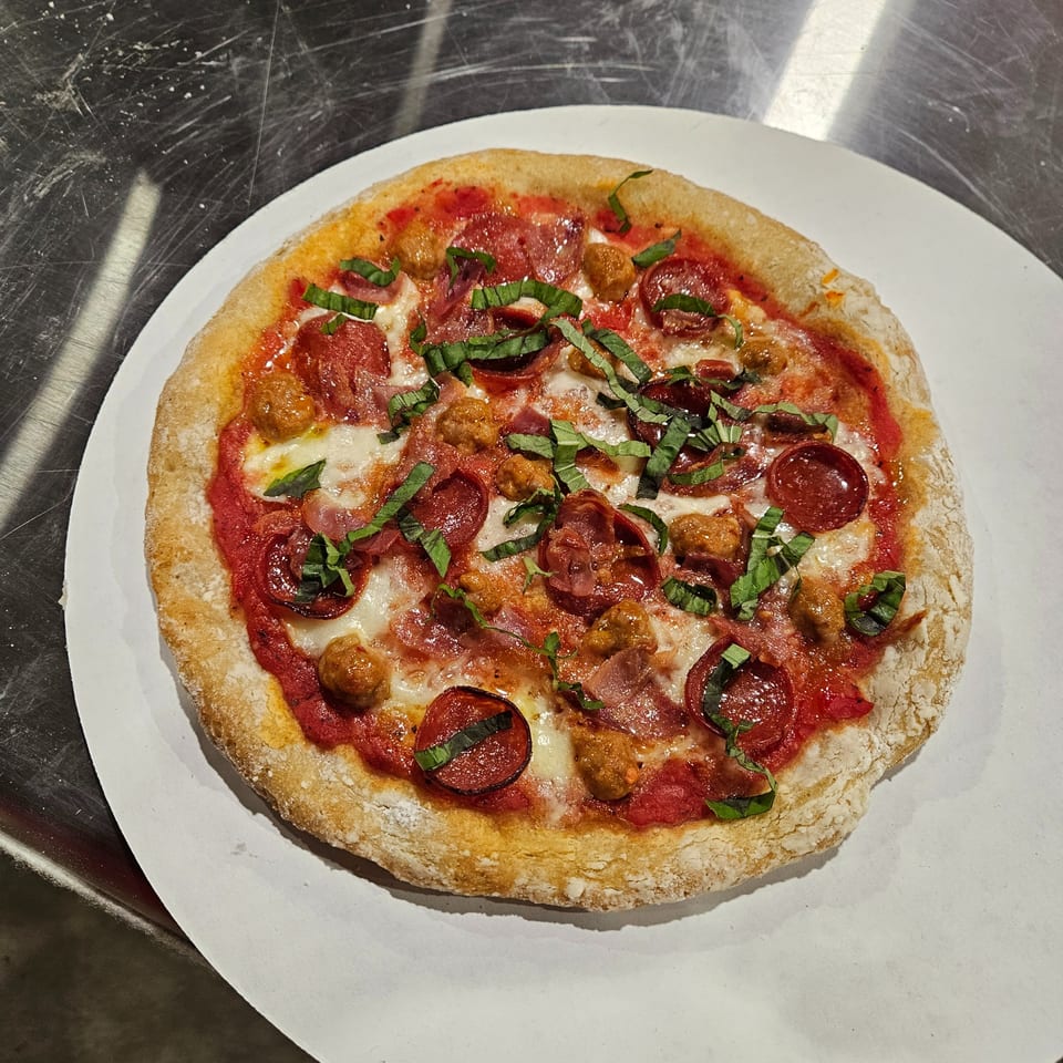 A Little Pizza Heaven's Italian pizza with pepperoni, sausage, and basil on a white plate.