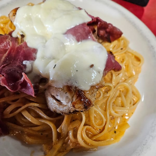 Creamy pasta dish with melted cheese, sliced meat, and grilled chicken on a white plate.