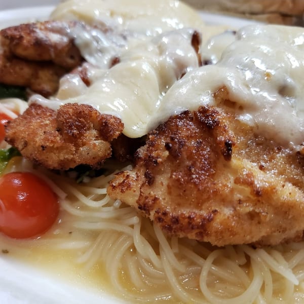 Crispy chicken cutlets topped with creamy white sauce, served over spaghetti with cherry tomatoes.
