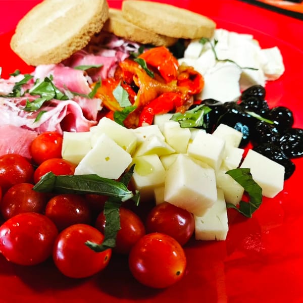 A vibrant Italian antipasto platter with prosciutto, cheeses, tomatoes, olives, roasted peppers, and bread.